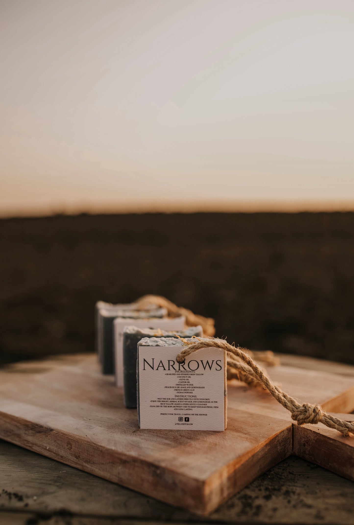 Till & Tallow Narrows soap-on-a-rope bars displayed on a wooden board with a rope handle, set against a warm prairie sunset background