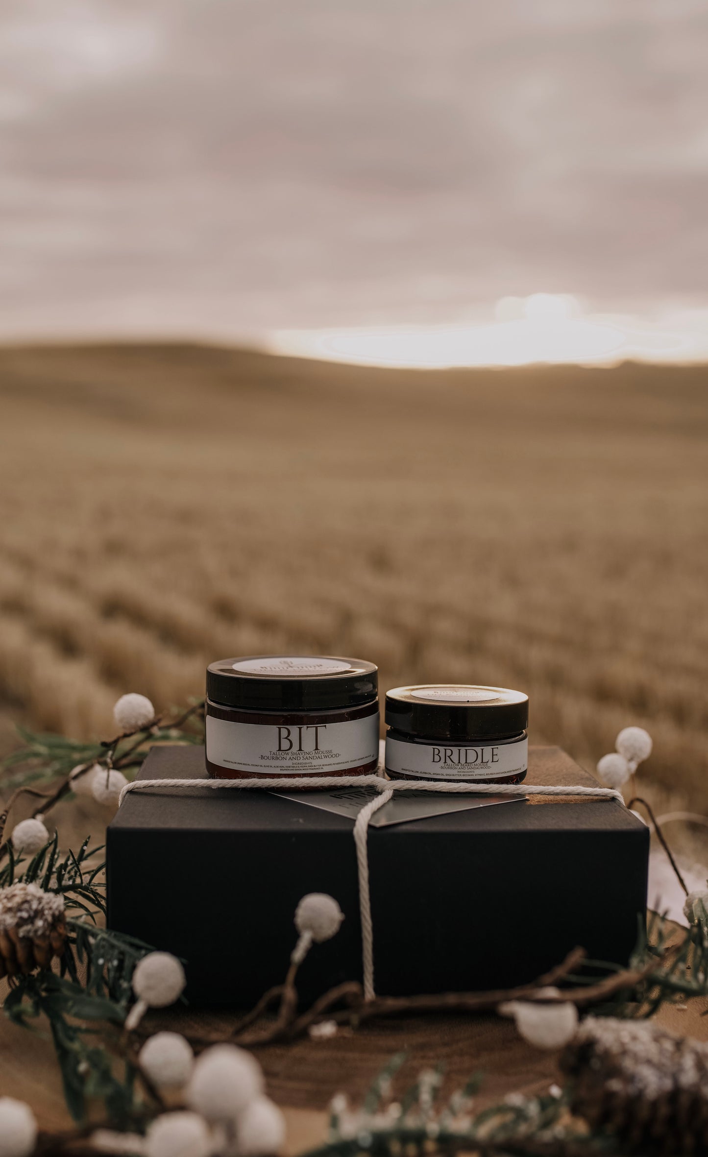 Bit & Bridle Tallow Body Butter - dark jars with white labels tied in twine on a prairie backdrop.