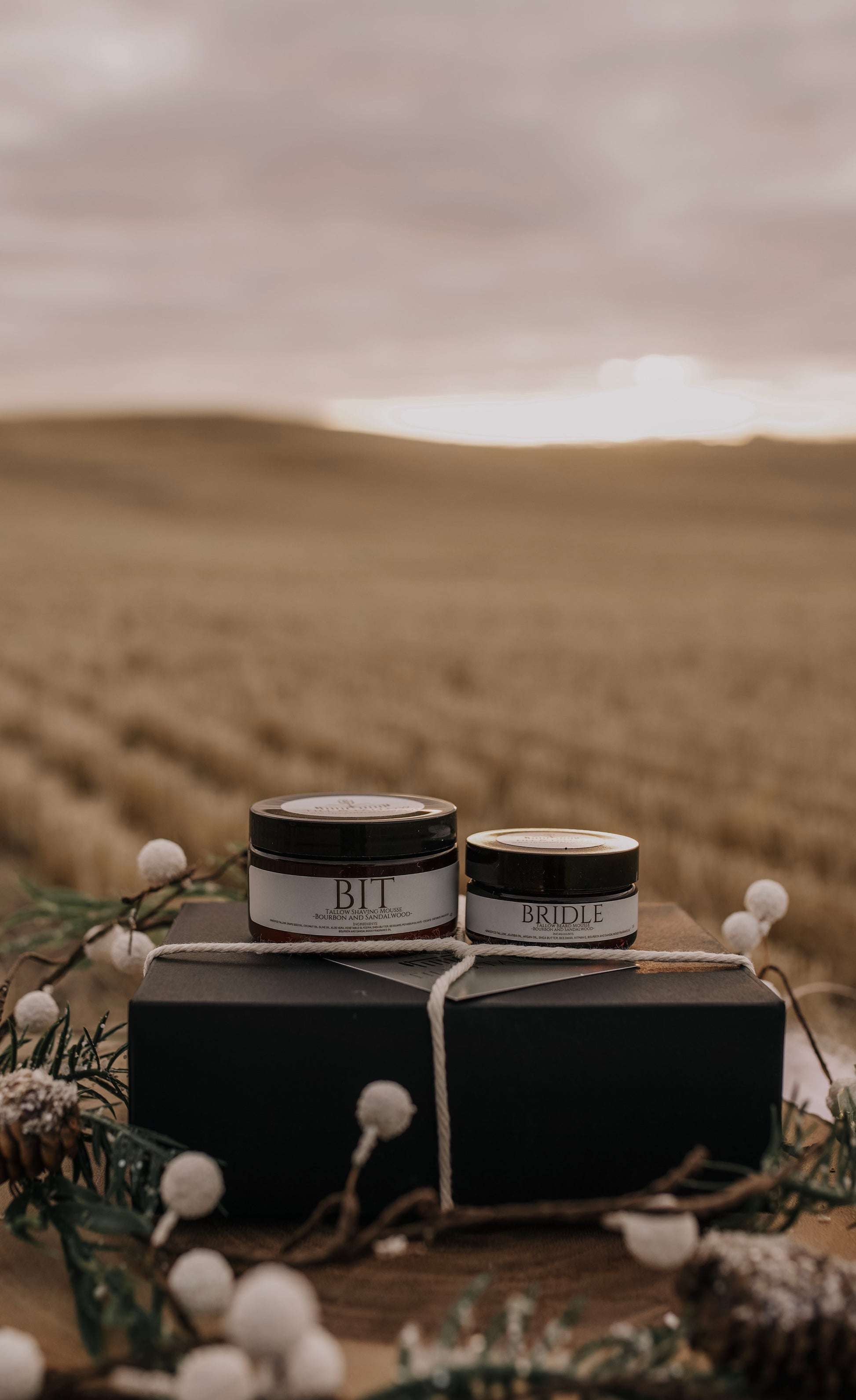 Bit & Bridle Tallow Body Butter - dark jars with white labels tied in twine on a prairie backdrop.