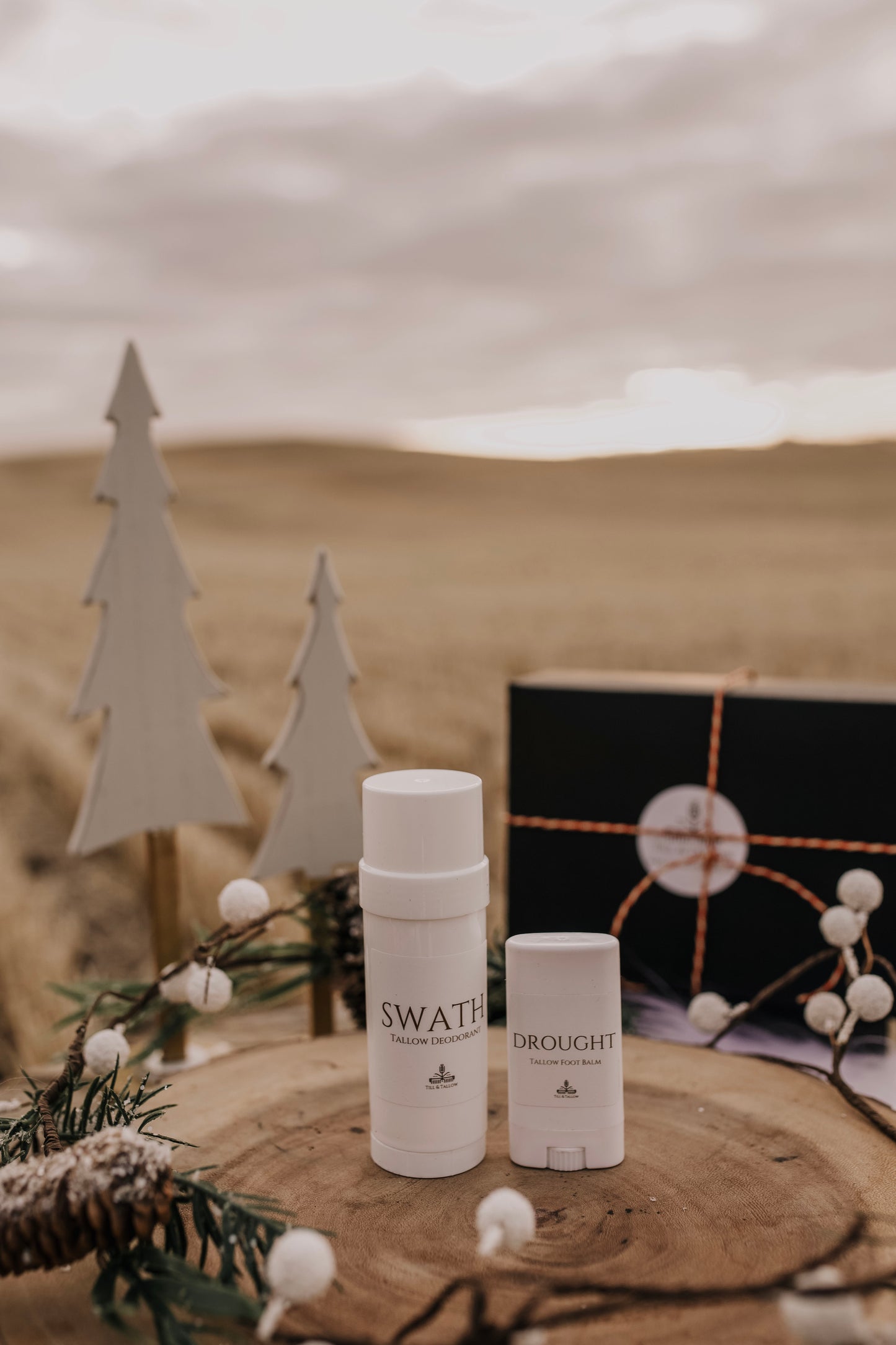Till & Tallow Swath deodorant and Drought heel balm on a rustic wooden display with winter accents.