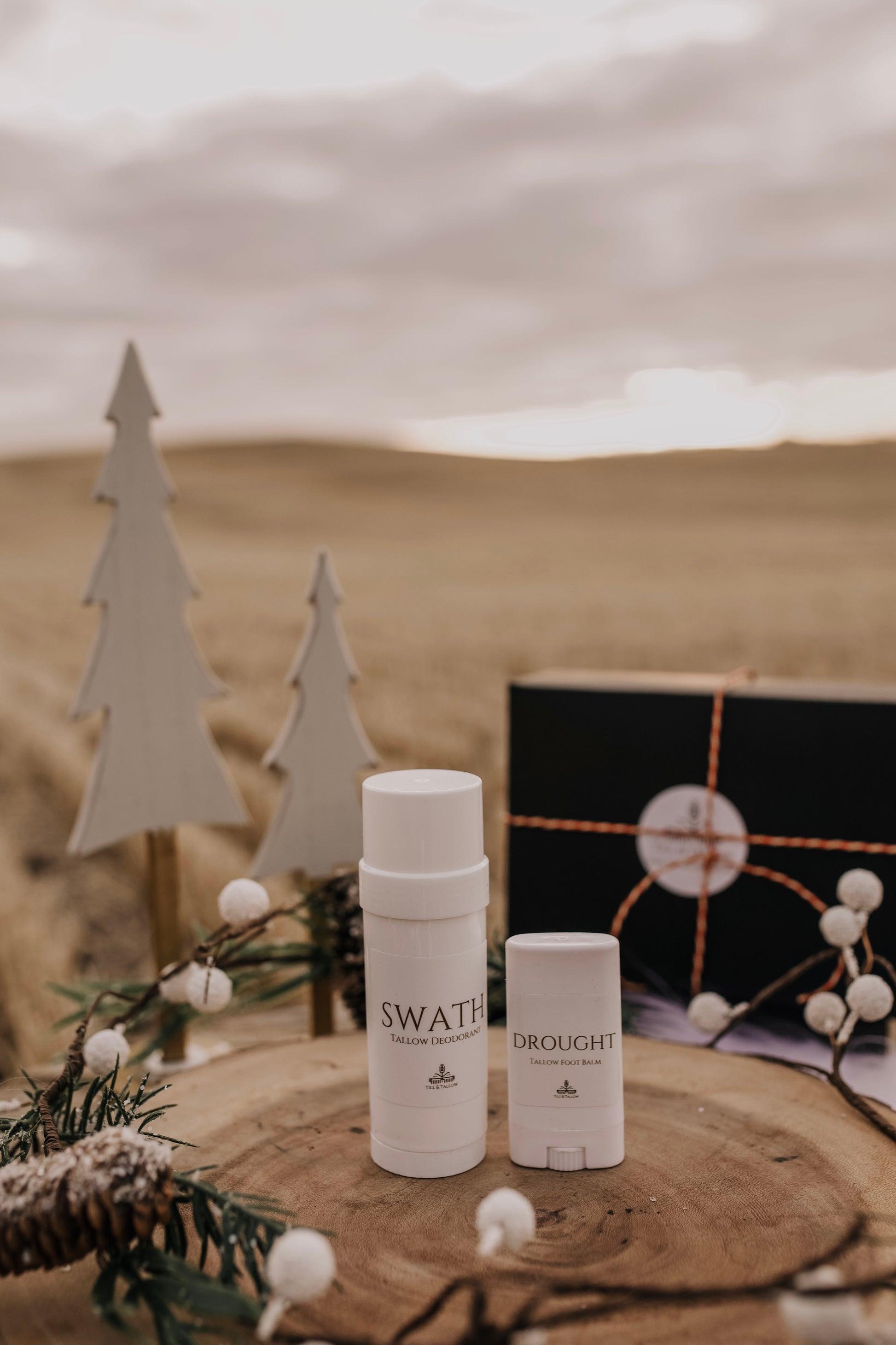 Till & Tallow Swath deodorant and Drought heel balm on a rustic wooden display with winter accents.