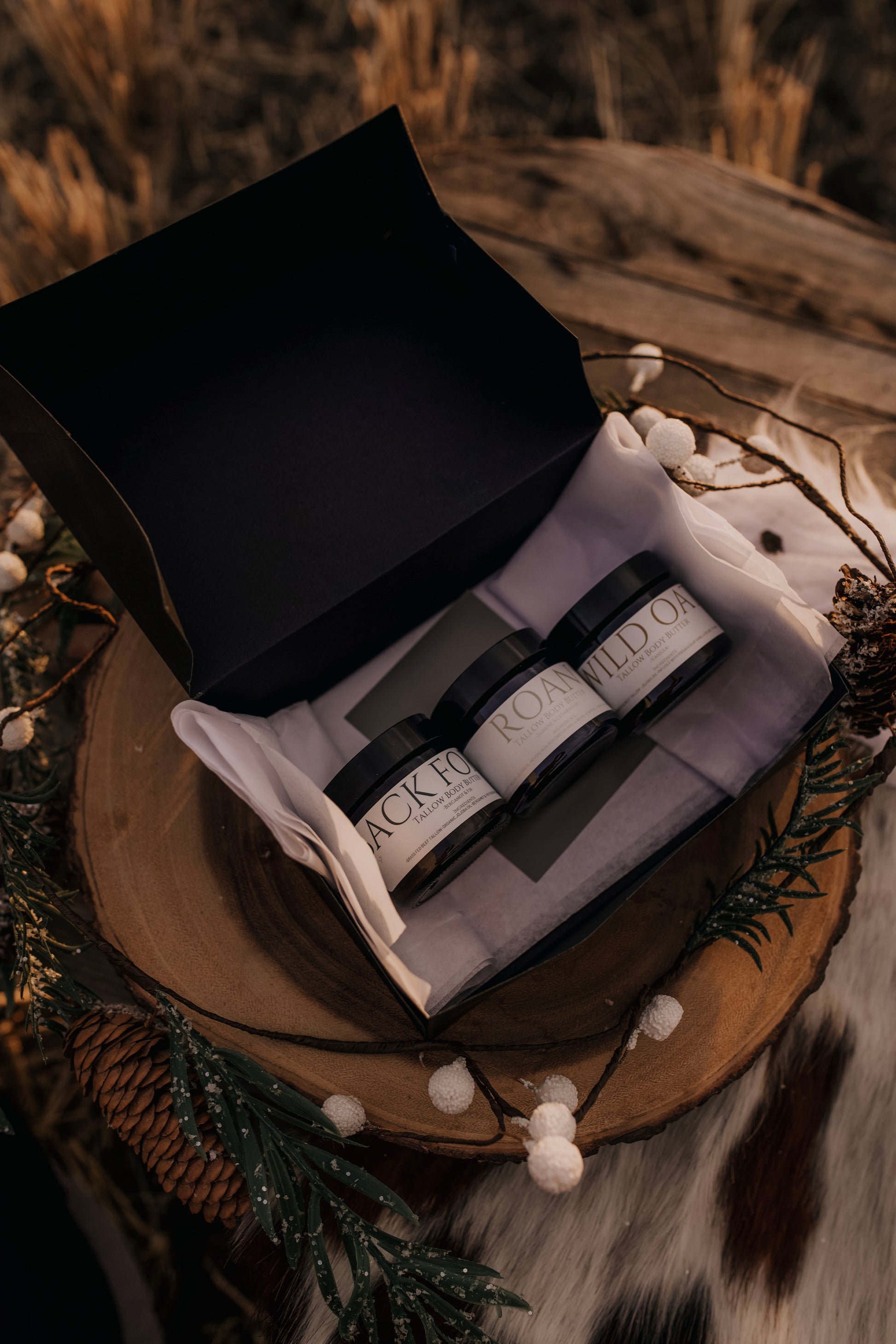 "Till & Tallow 3-pack body butter gift box displayed on a rustic wooden tray with pine decor and natural holiday elements"
