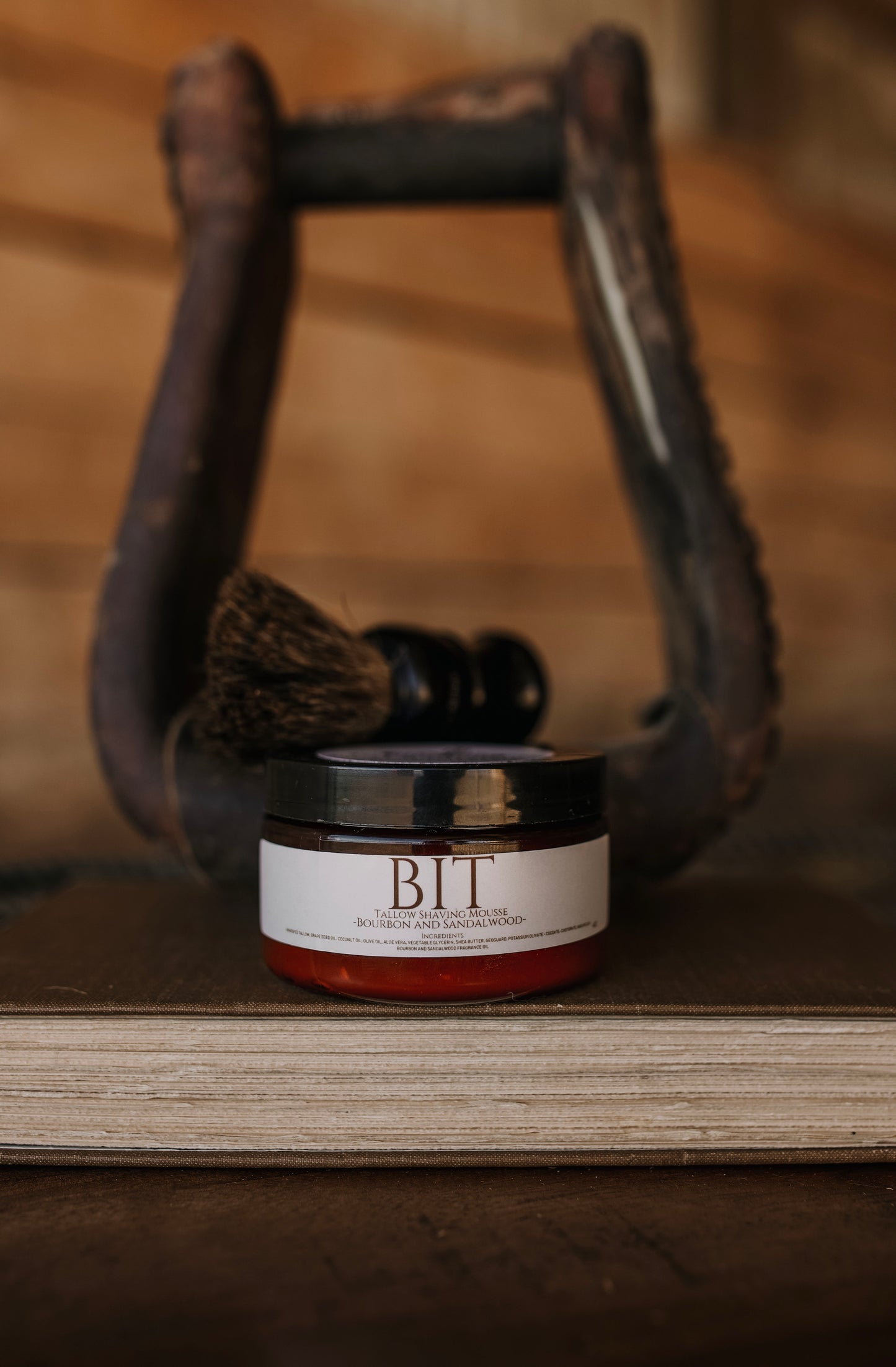 Till & Tallow Bit Shaving Mousse in amber jar displayed inside a rustic horse stirrup, handcrafted in Alberta