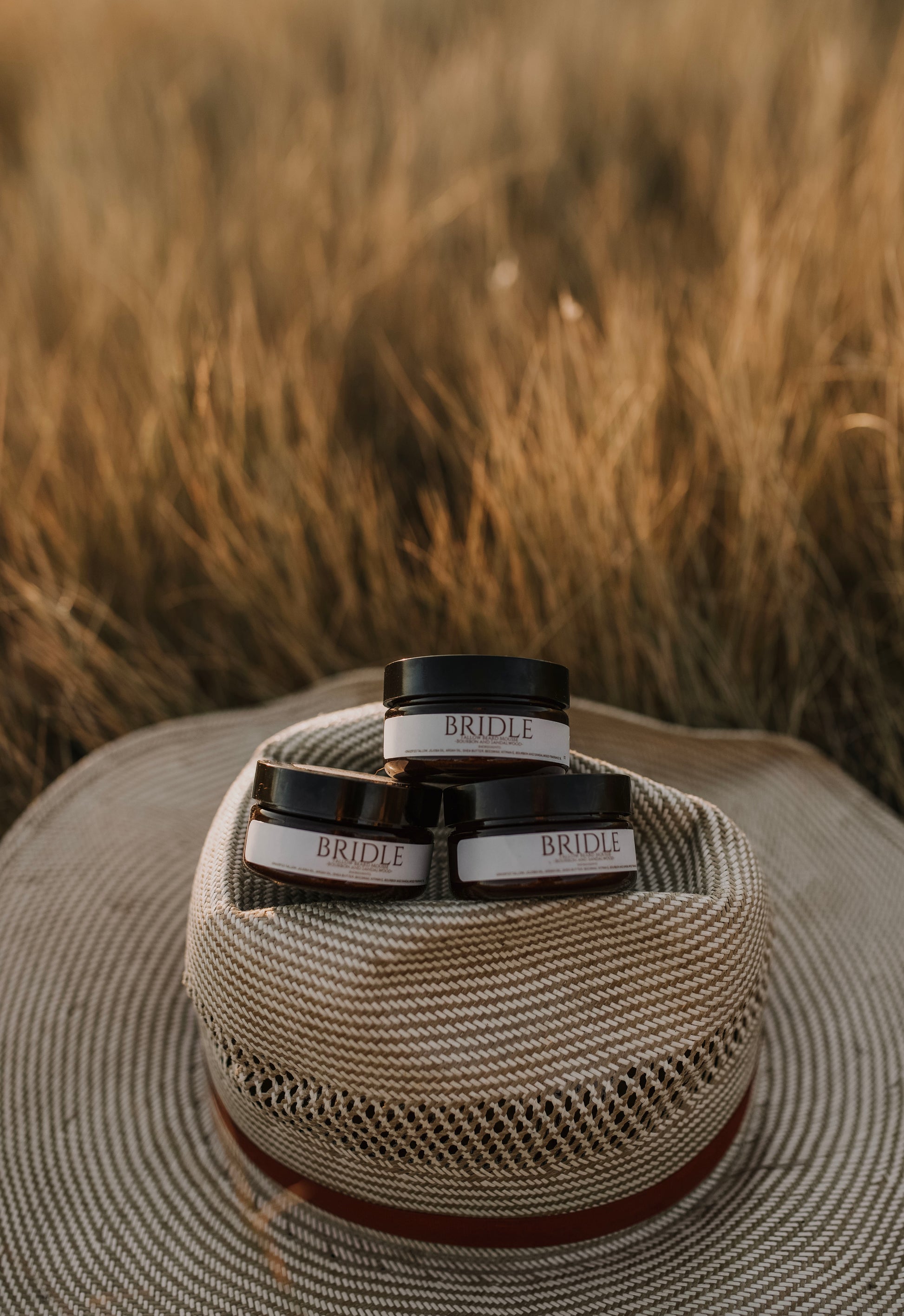 Till & Tallow Bridle Beard Mousse jars stacked on a cowboy hat with a rustic outdoor background, handcrafted in Alberta
