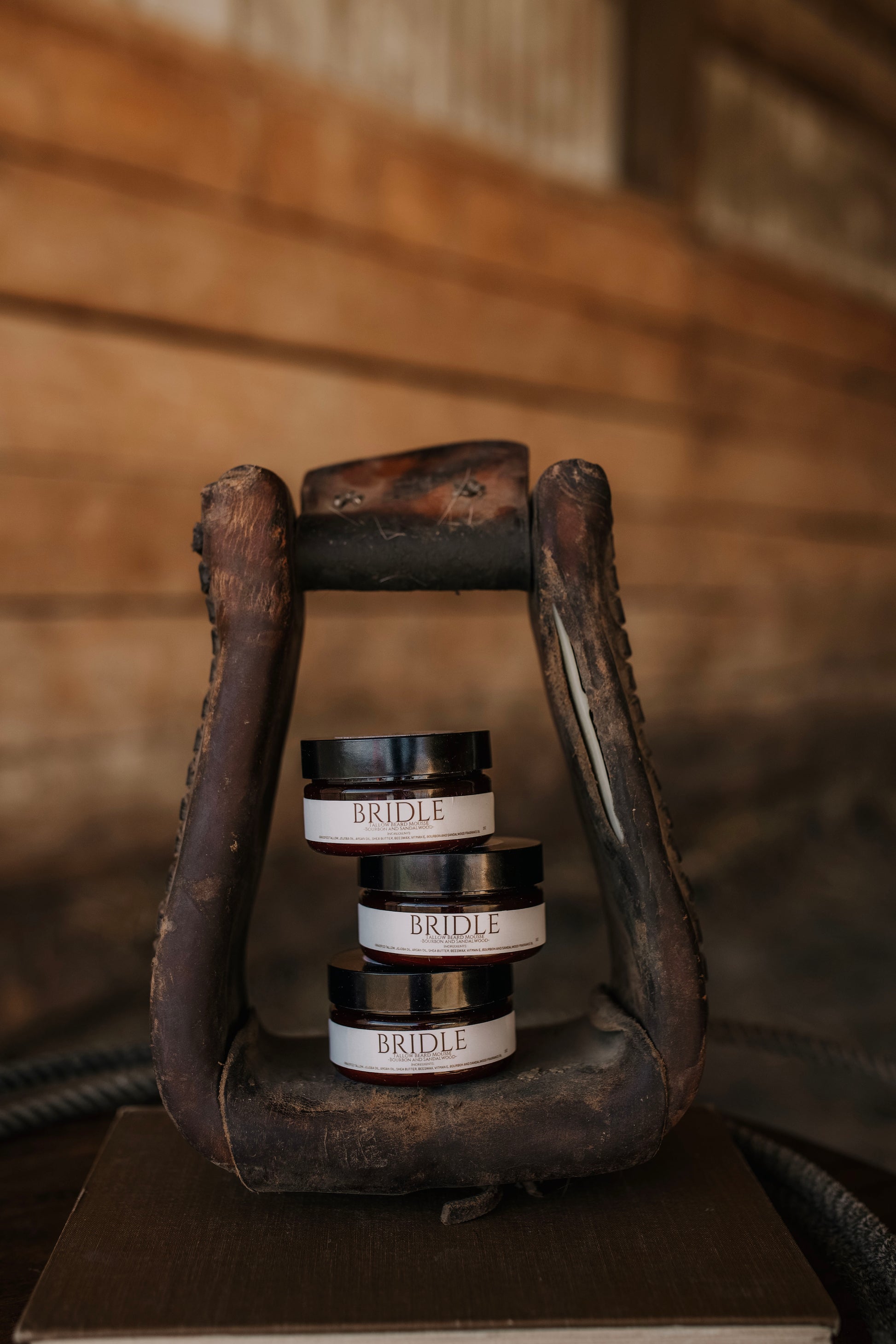 Till & Tallow Bridle Beard Mousse jars stacked inside a rustic horse stirrup, handcrafted in Alberta