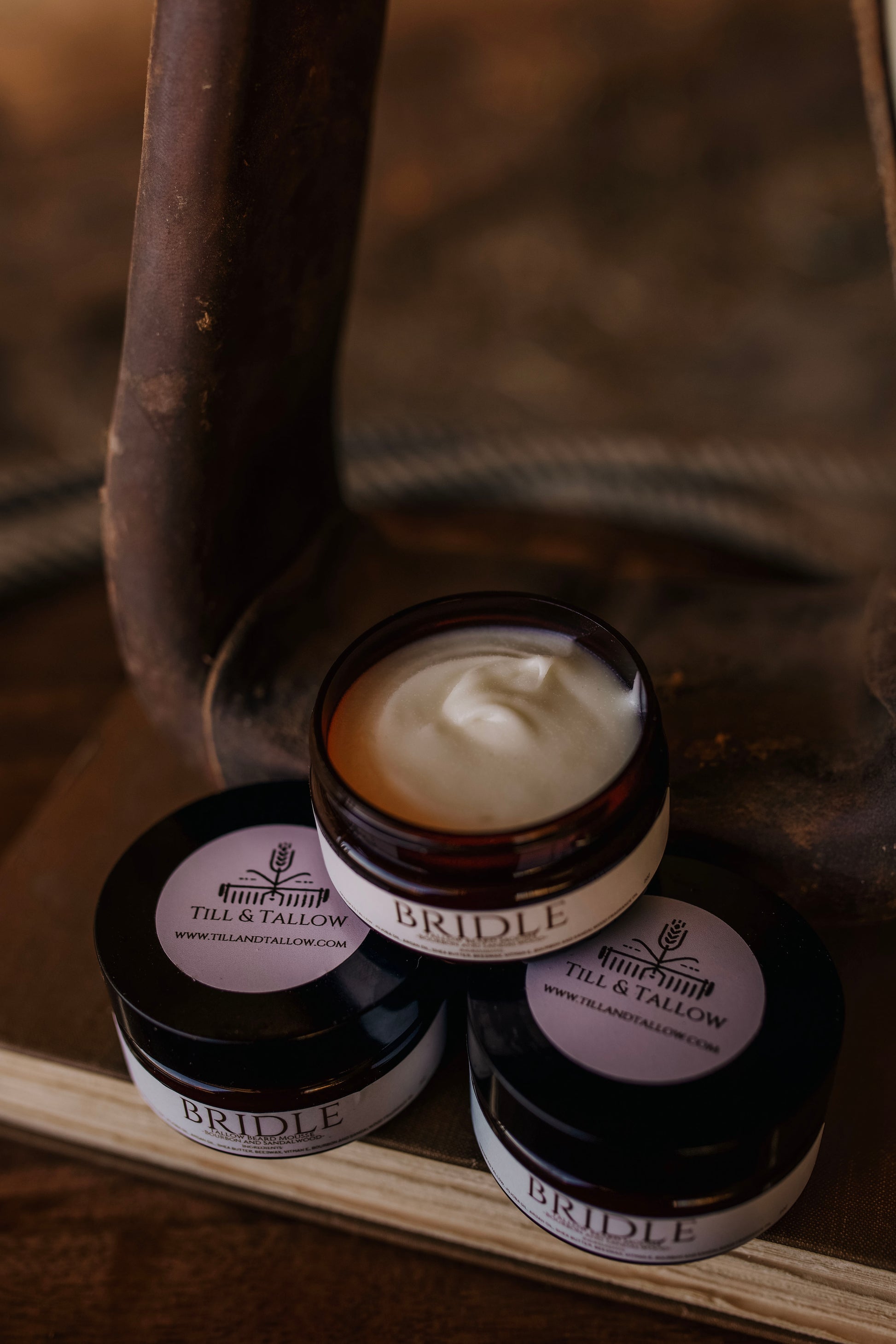Till & Tallow Bridle Beard Mousse jars displayed on a wooden surface with rustic natural lighting, handcrafted in Alberta.
