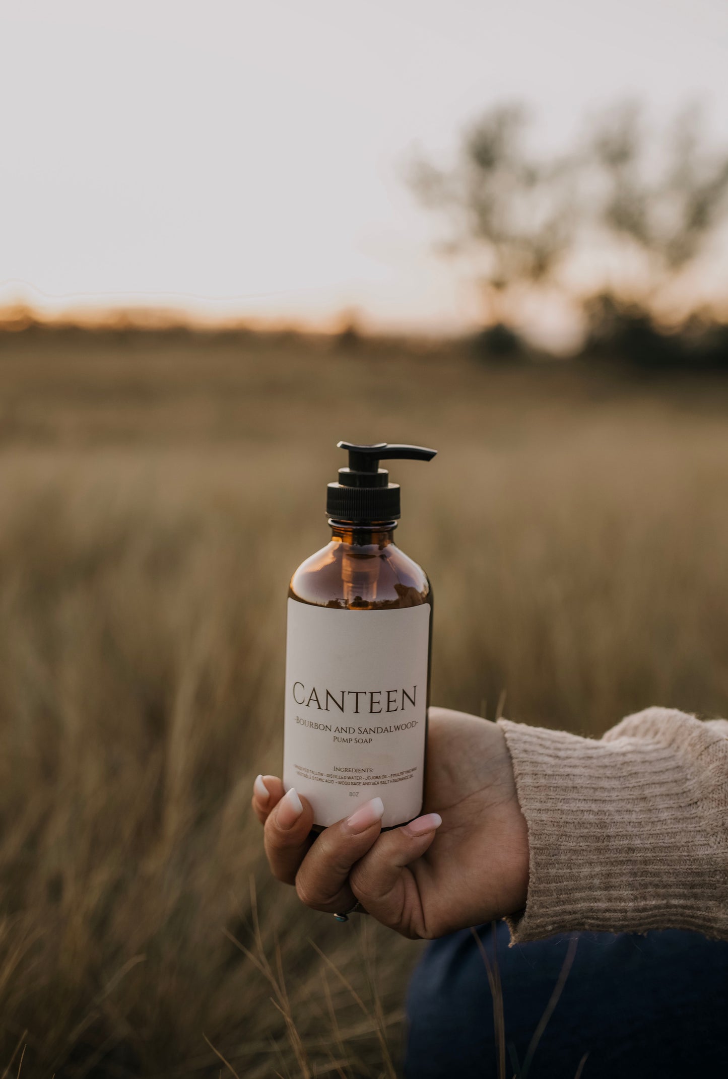 Till & Tallow Canteen Liquid Hand Soap bottle held in hand outdoors with a blurred Alberta field background, captured in natural light.
