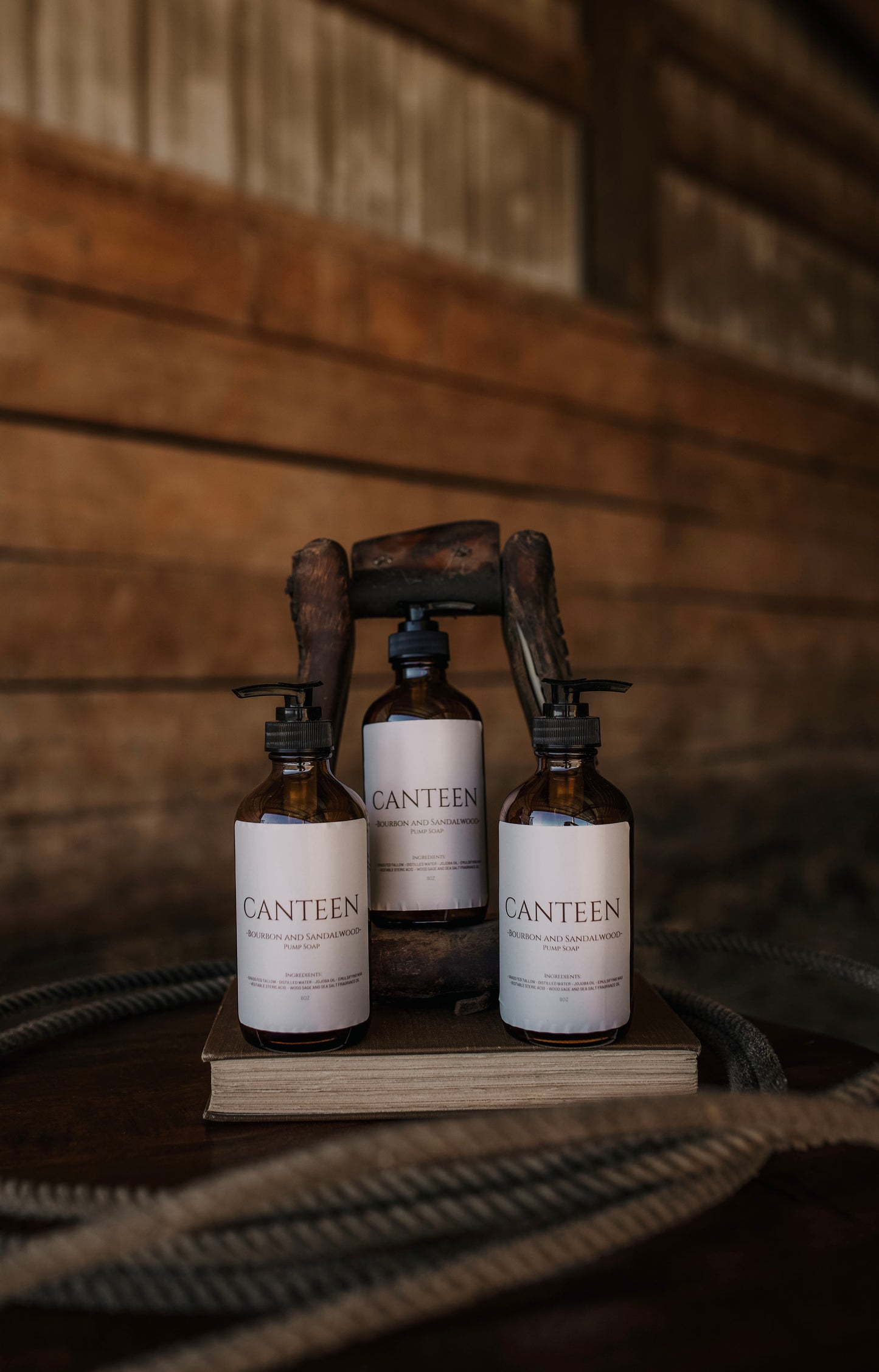 Till & Tallow Three Canteen Liquid Hand Soap Bottles arranged on a rustic wooden table with a blurred barn background