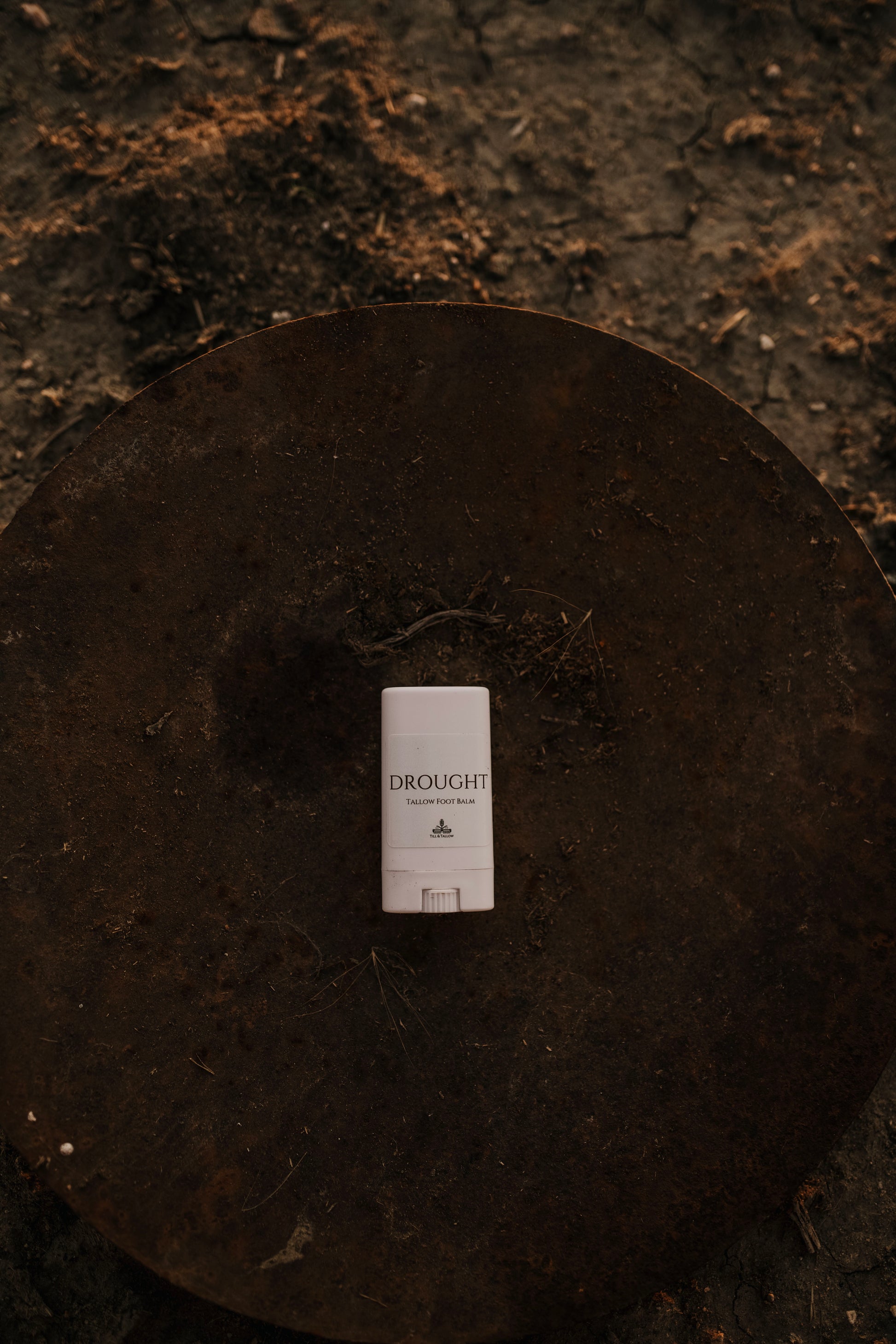 Till & Tallow Drought Cracked Heel Balm stick in white tube displayed on a rustic dark metal disk, handcrafted in Alberta, Canada
