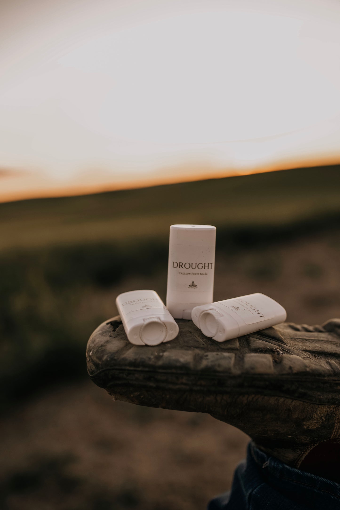 Three Till  & Tallow Drought Cracked Heel Balm tubes resting on boot sole with a prairie sunset background, handcrafted in Alberts