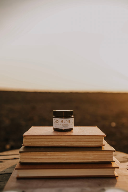 Till & Tallow Grounded Seborrheic-safe Face Balm sitting on a stack of books outdoors with a soft prairie background, handcrafted in Alberta