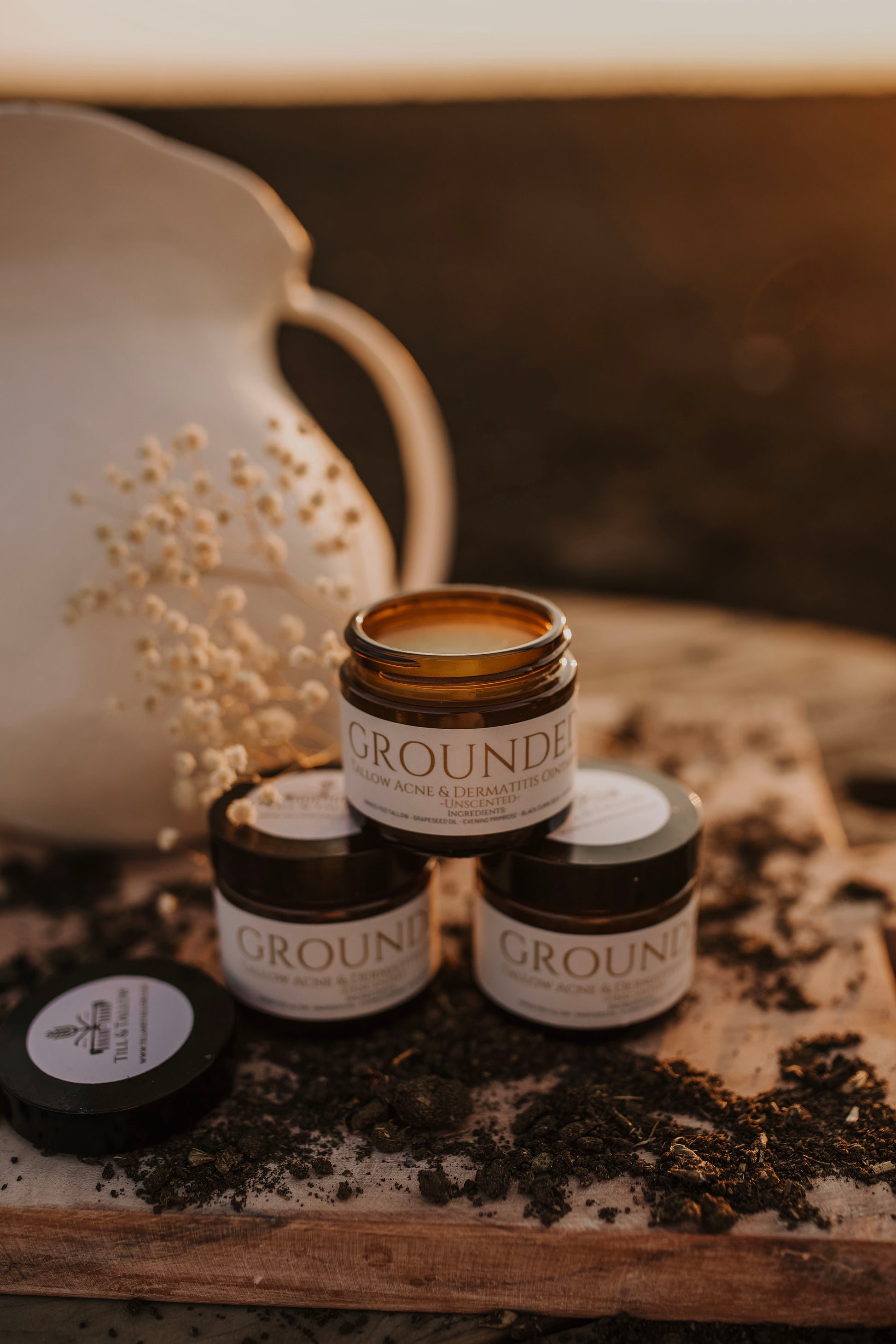 Till & Tallow jars of Grounded Seborrheic-Safe Face Balm displayed on a rustic wooden surface with pottery and natural light in the background, handcrafted in Alberta