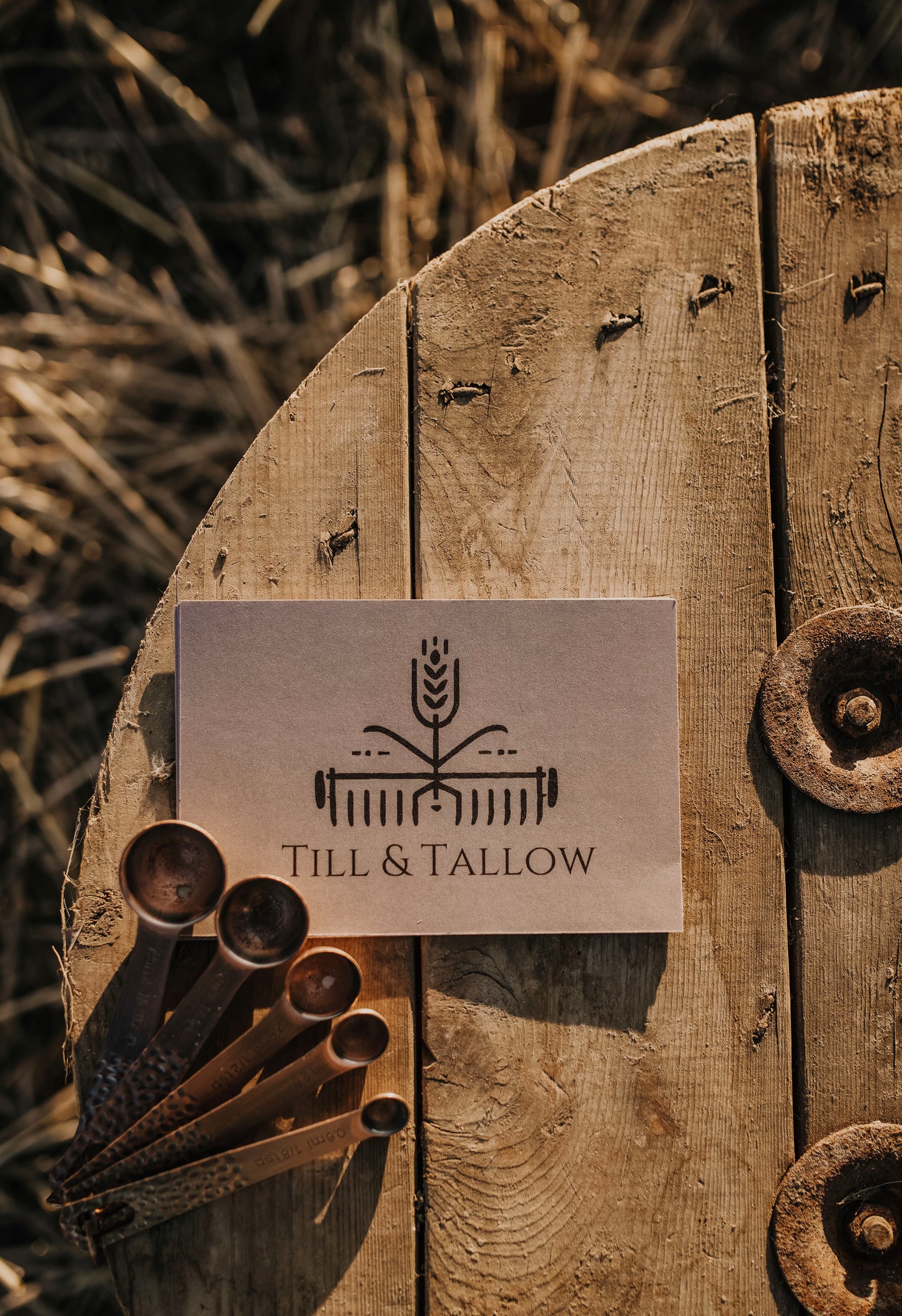 Till & Tallow logo card displayed on a rustic wood with vintage brass measuring spoons