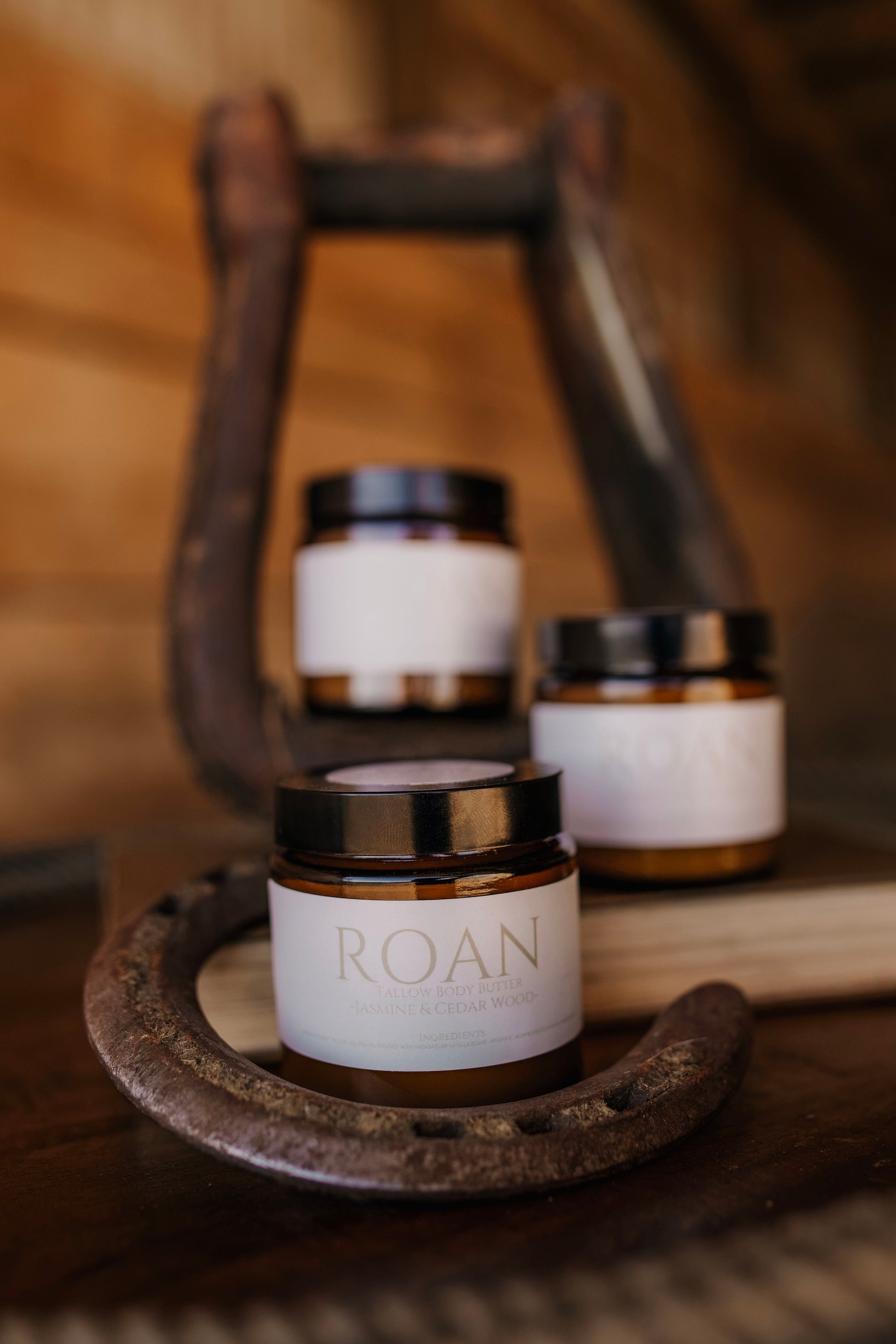 Till & Tallow Roan Body Butter jars stacked inside a horse stirrup on a rustic wooden surface, handcrafted in Alberta.