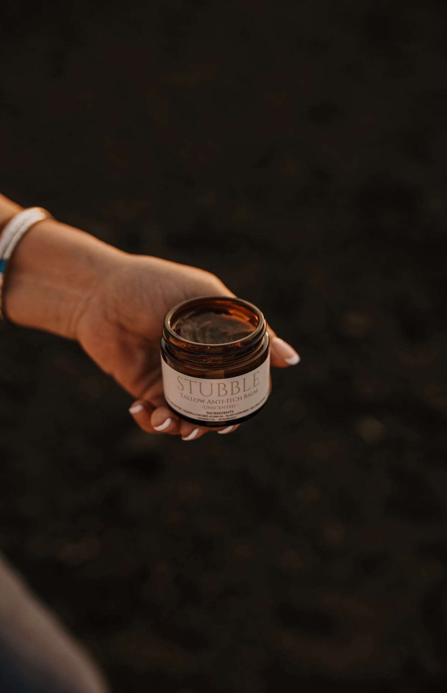 Till & Tallow Stubble Anti-Itch Balm held in a hand against a dark natural background showing the creamy tallow texture, handcrafted in Alberta
