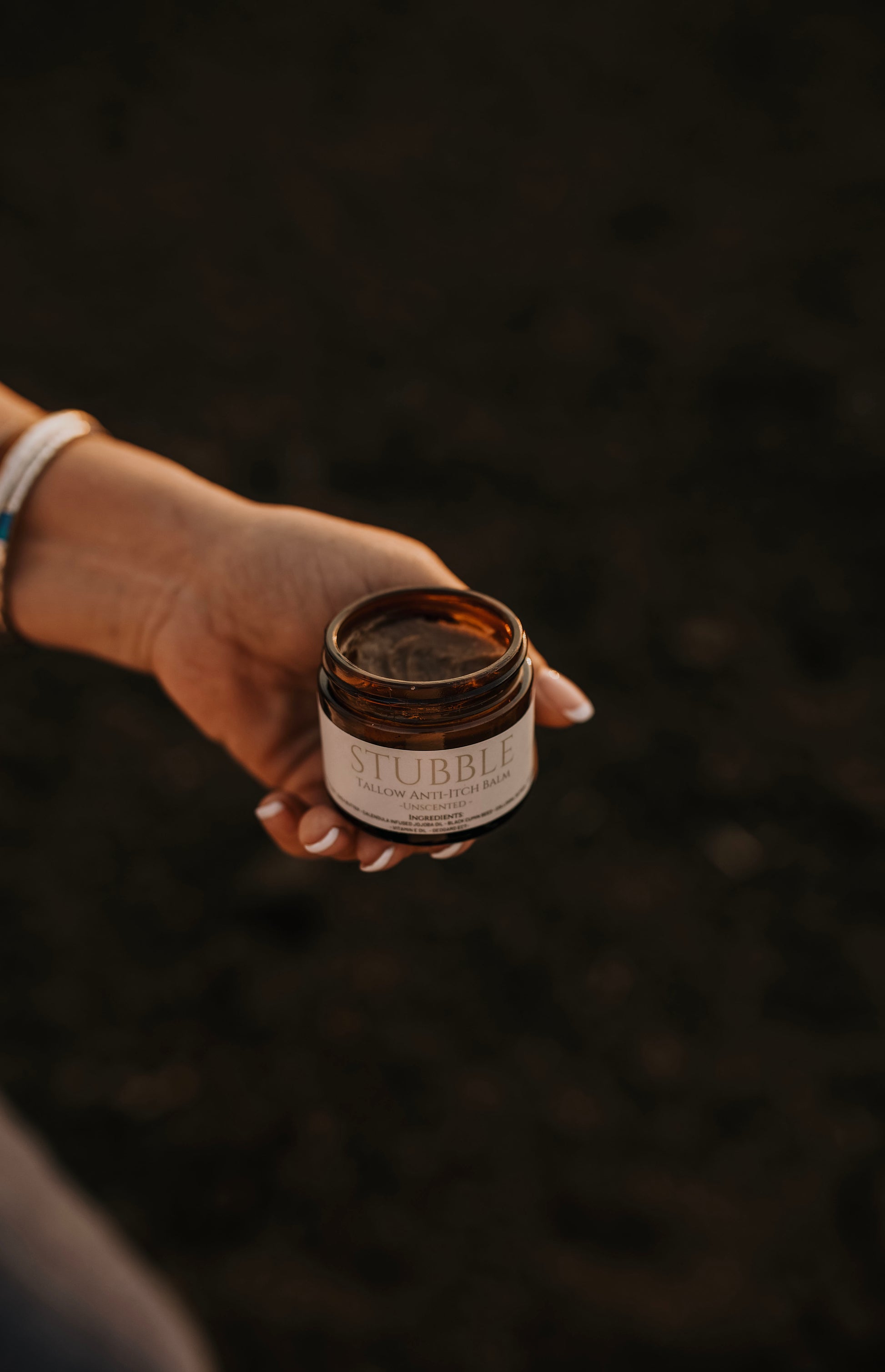 Till & Tallow Stubble Anti-Itch Balm held in a hand against a dark natural background showing the creamy tallow texture, handcrafted in Alberta