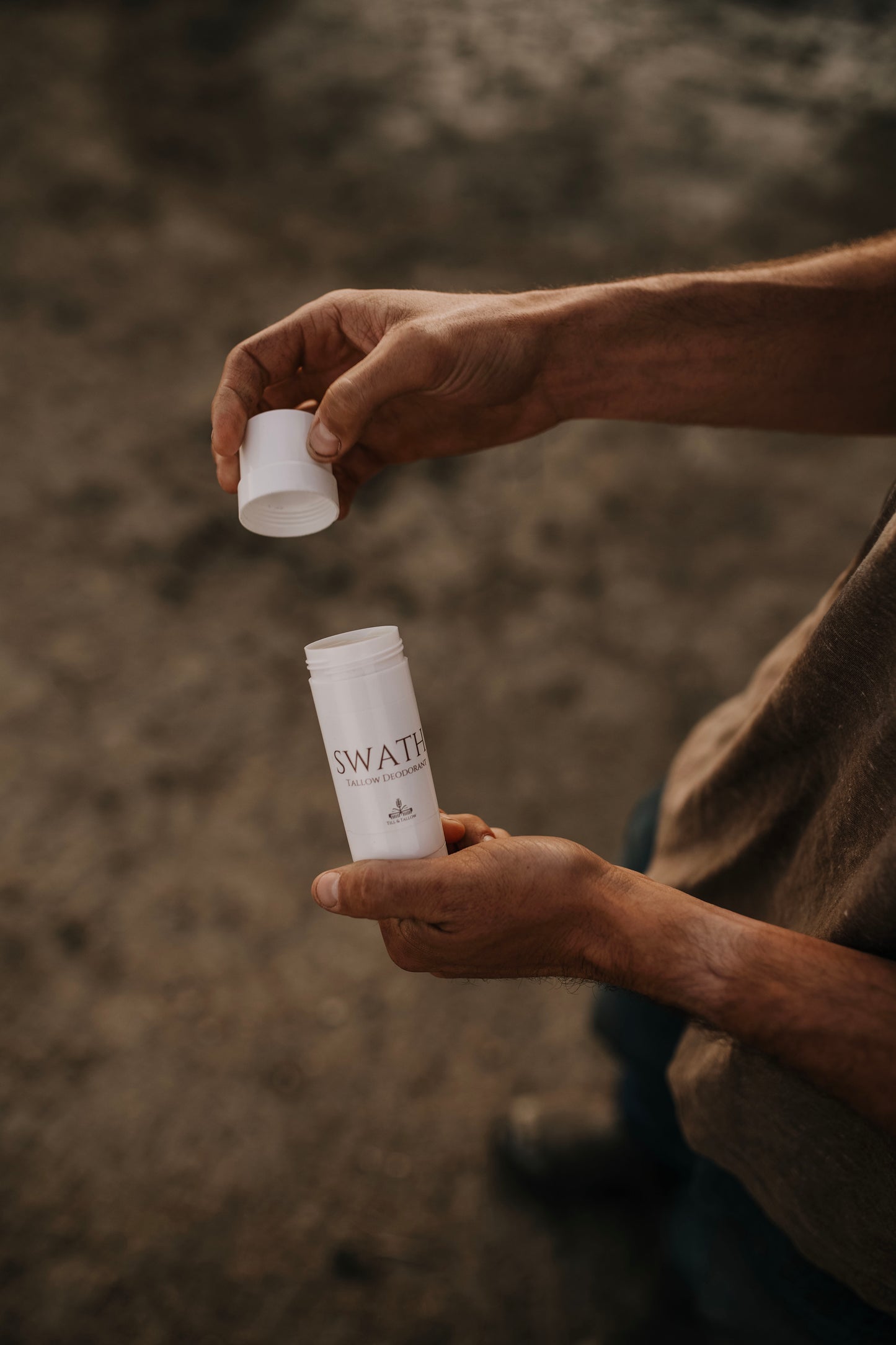 Till & Tallow SWATH natural deodorant held in both hands outdoors, lid removed to show texture, with a soft blurred natural background, handcrafted in Alberta.