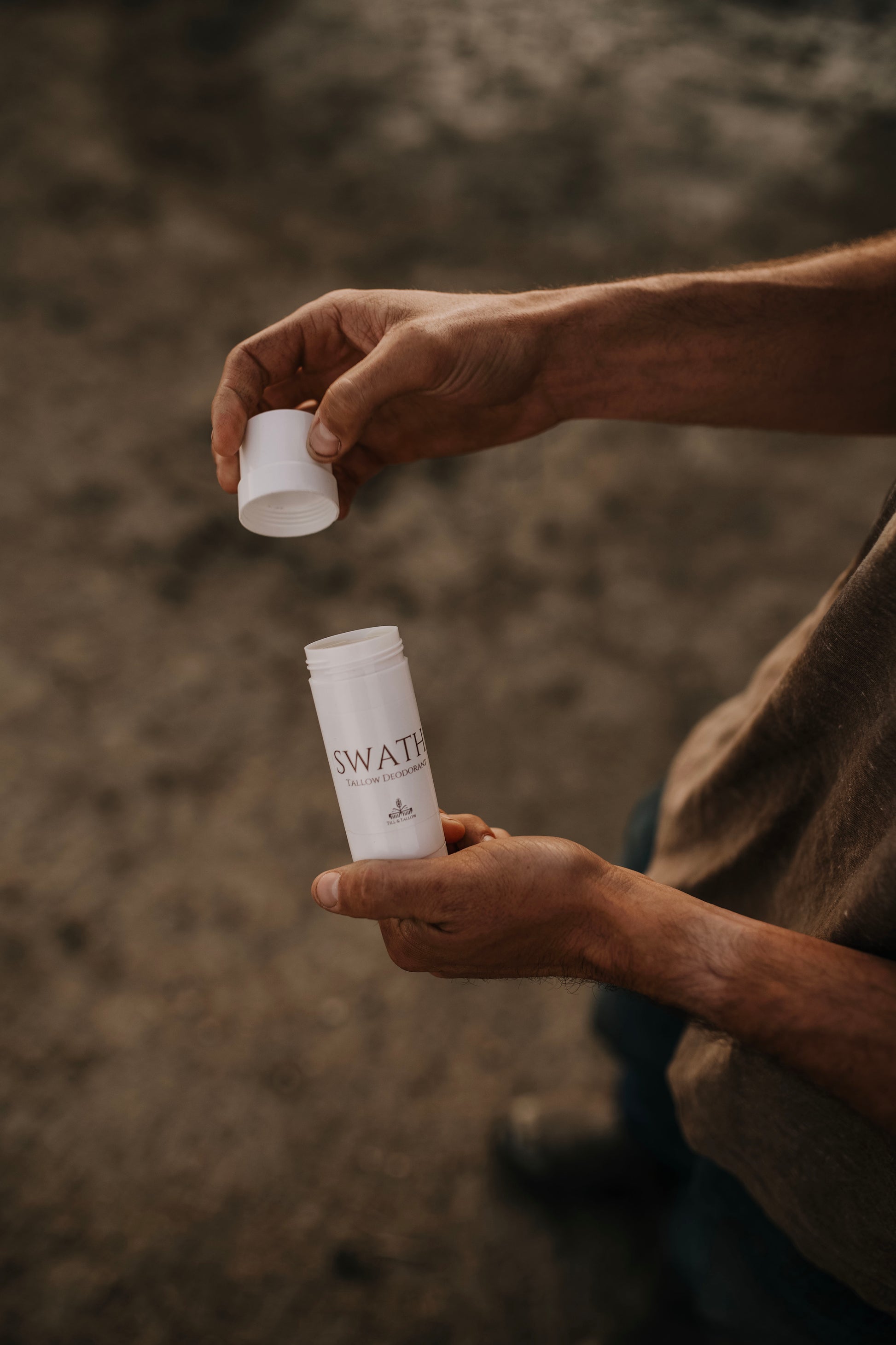Till & Tallow SWATH natural deodorant held in both hands outdoors, lid removed to show texture, with a soft blurred natural background, handcrafted in Alberta.