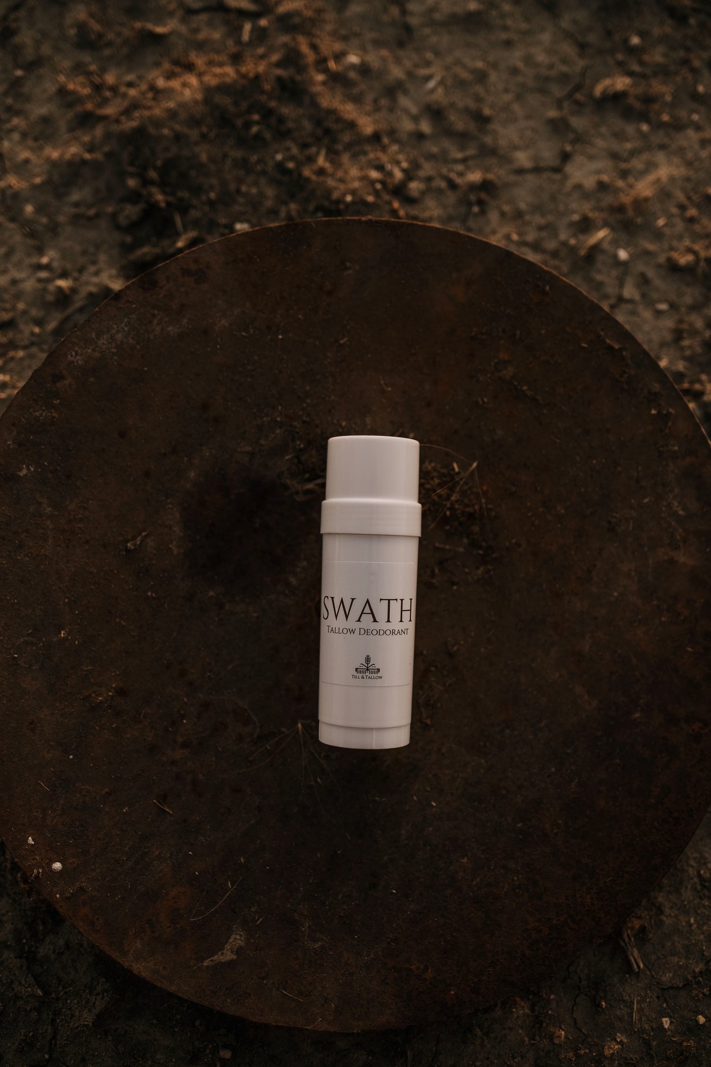 Till & Tallow SWATH deodorant stick in white tube resting on a rustic metal disk with warm natural lighting, handcrafted in Alberta.