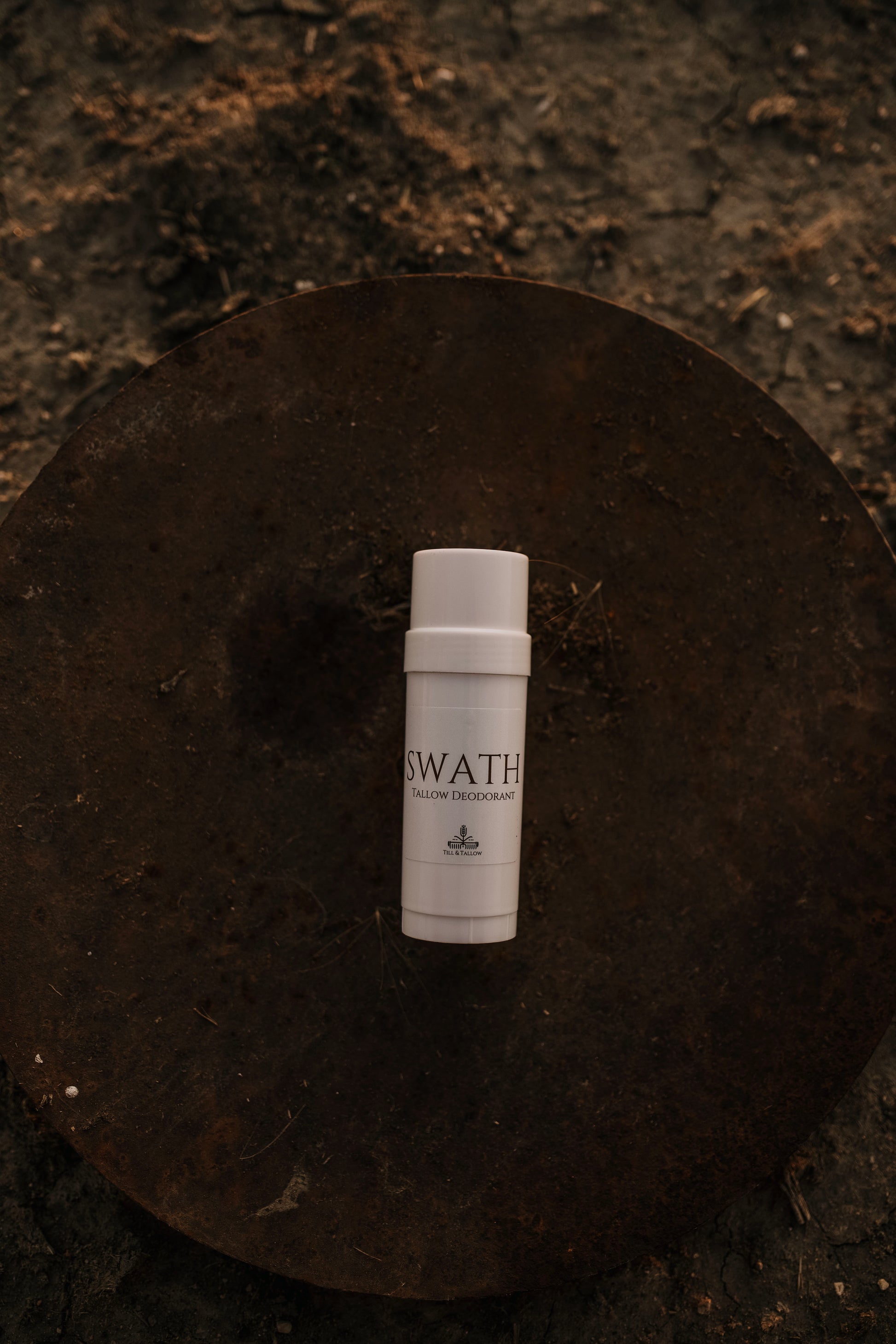 Till & Tallow SWATH deodorant stick in white tube resting on a rustic metal disk with warm natural lighting, handcrafted in Alberta.