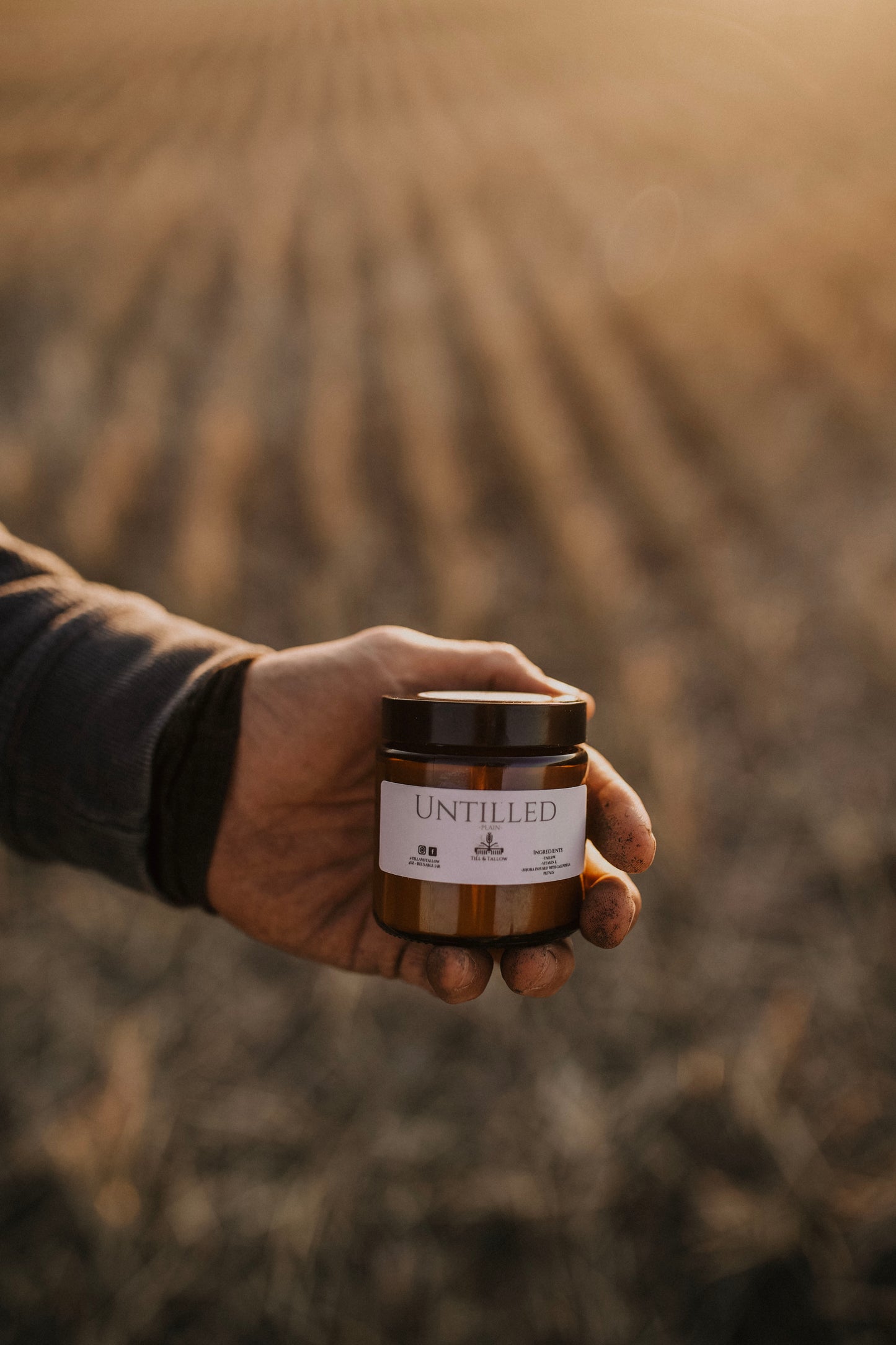 Till & Tallow Untilled Body Butter farmer holding jar in blurred farm field, handcrafted in Alberta