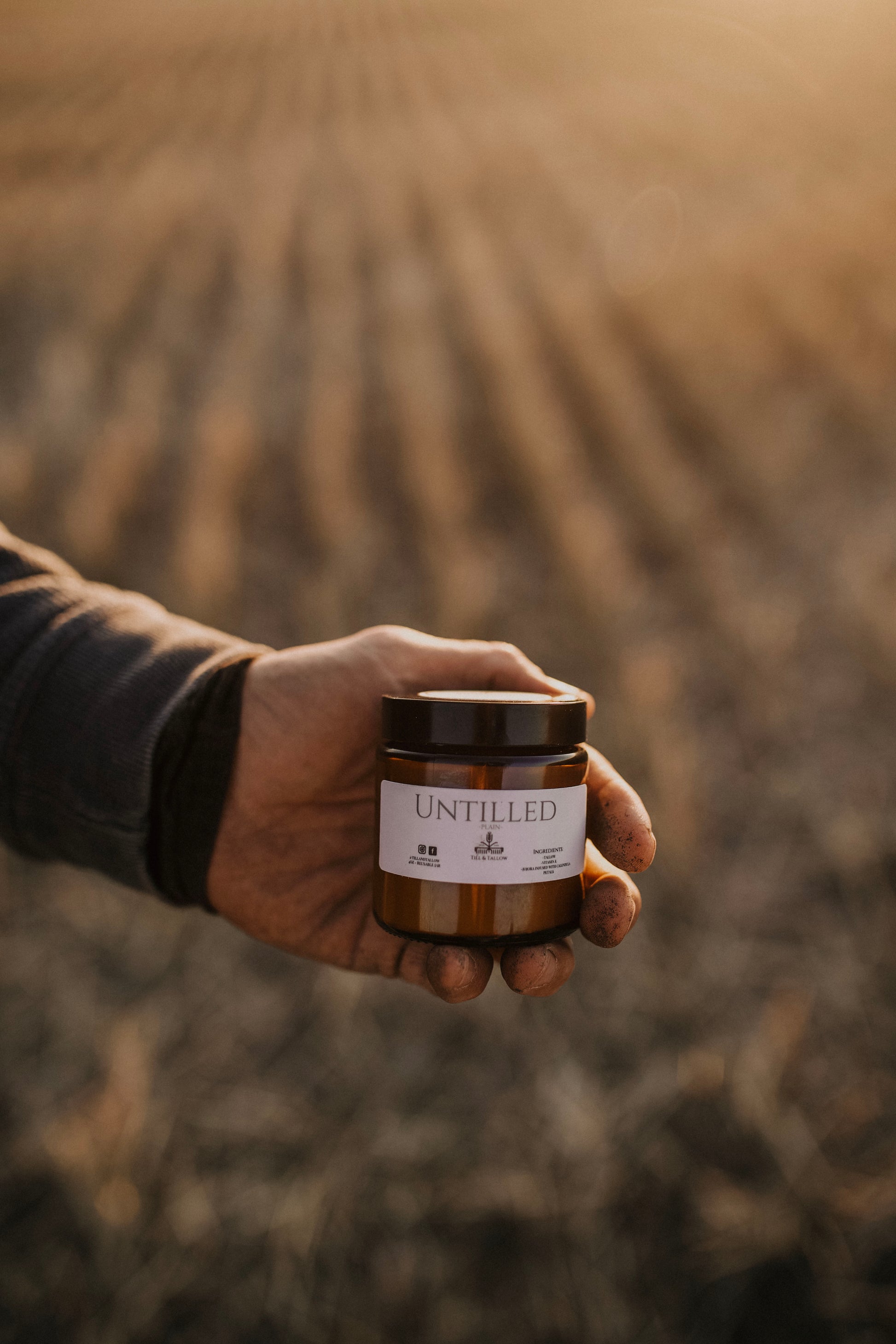 Till & Tallow Untilled Body Butter farmer holding jar in blurred farm field, handcrafted in Alberta